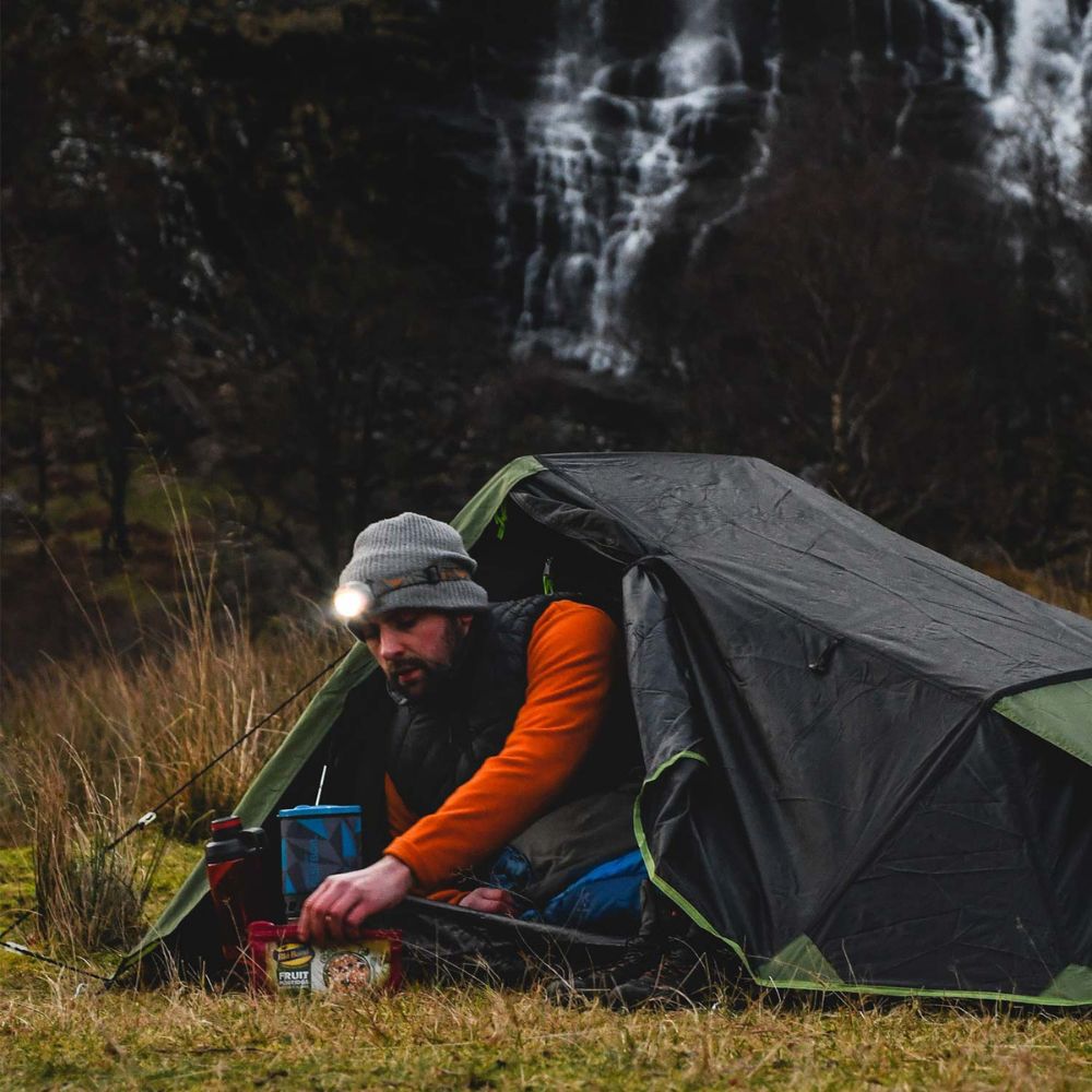 Camper using blade fastboil 3 gas stove outside a tent.