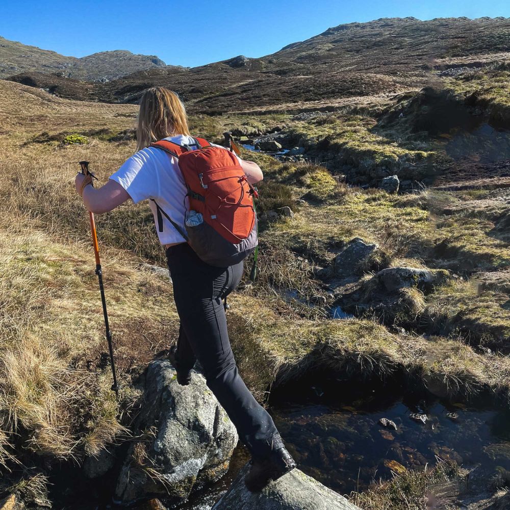 Side view of Venture Backpack 20L in rust/grey during hiking.