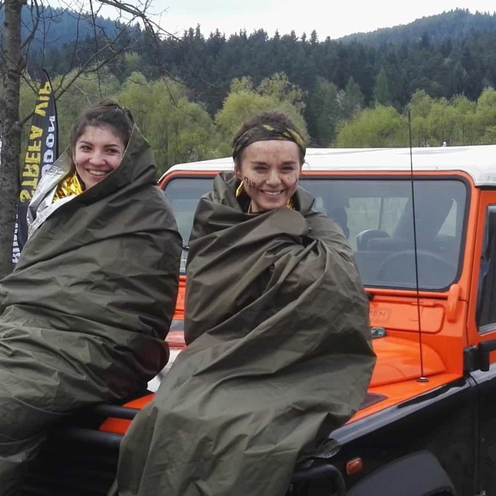 Two women wrapped in thermo-tarps sitting on a vehicle.