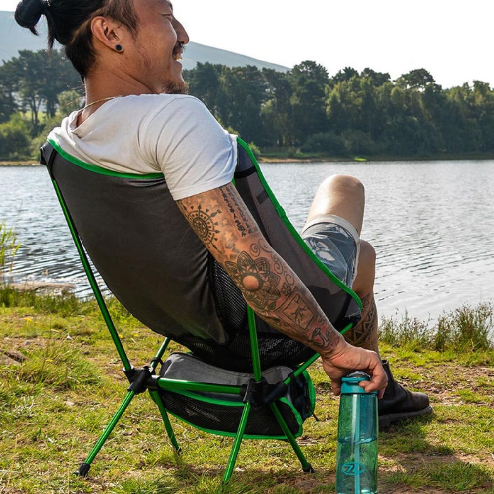 A person sits in a Highlander Ayr Folding Camping Chair by a lake, enjoying the scenery.