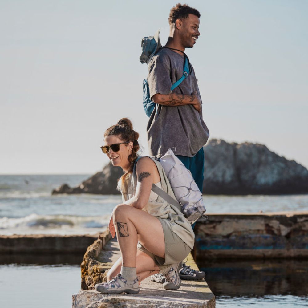 A woman crouches on a cement dock wearing KEEN Newport H2 sandals.