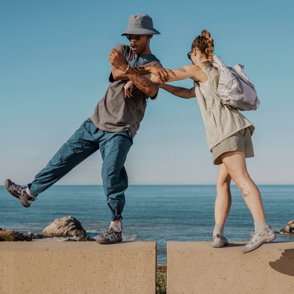 Two people balancing on a stone wall by the sea, wearing KEEN Newport sandals.