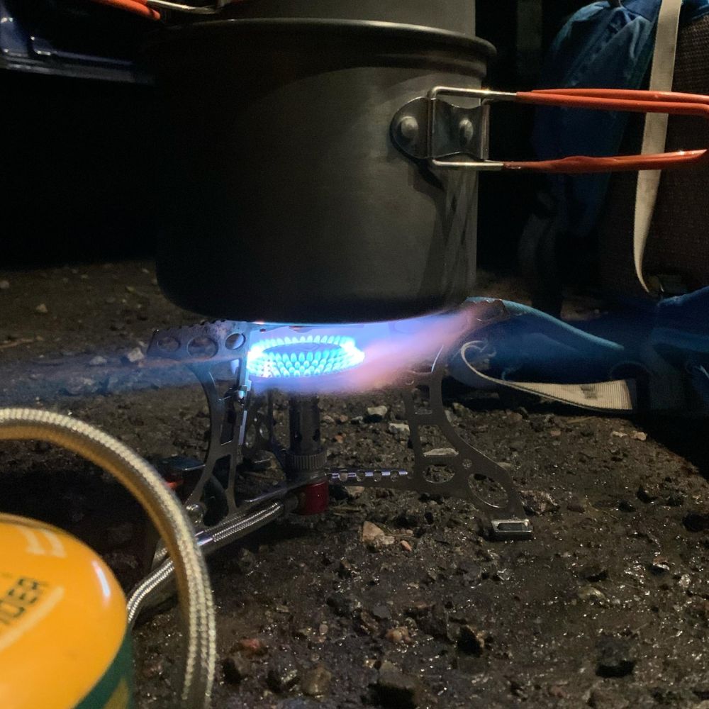 Camping gas stove in use outdoors with a pot and gas canister.