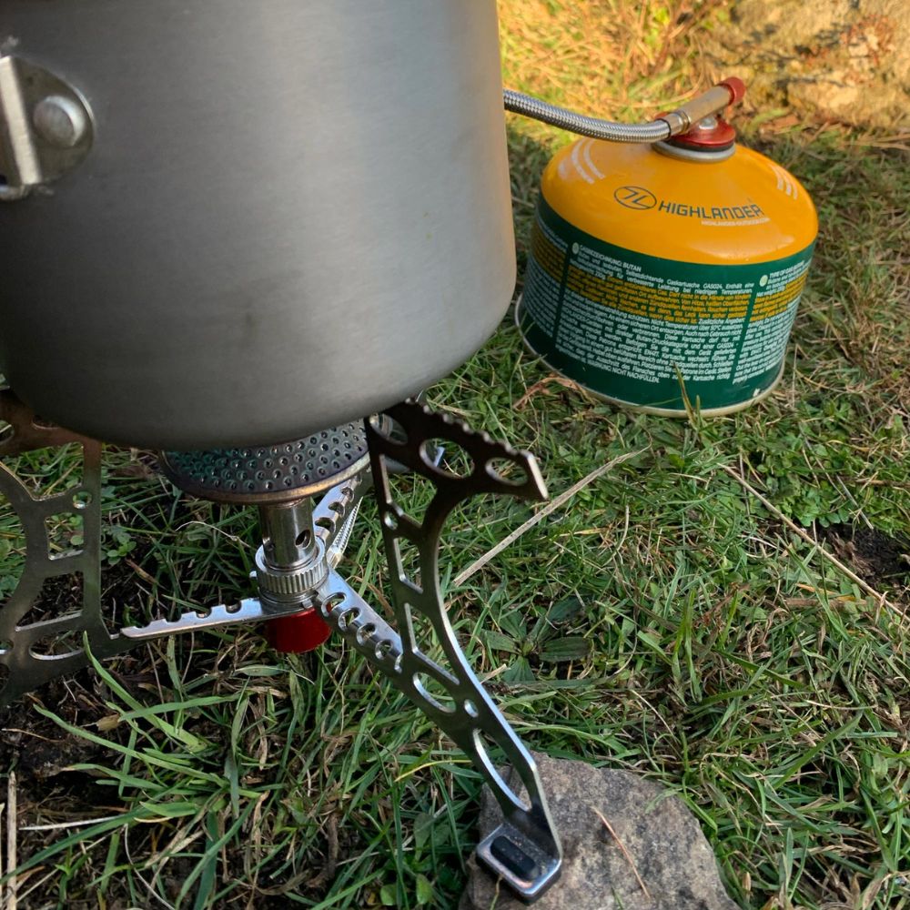 Triplex Compact Camping Gas Stove with pot in a field.